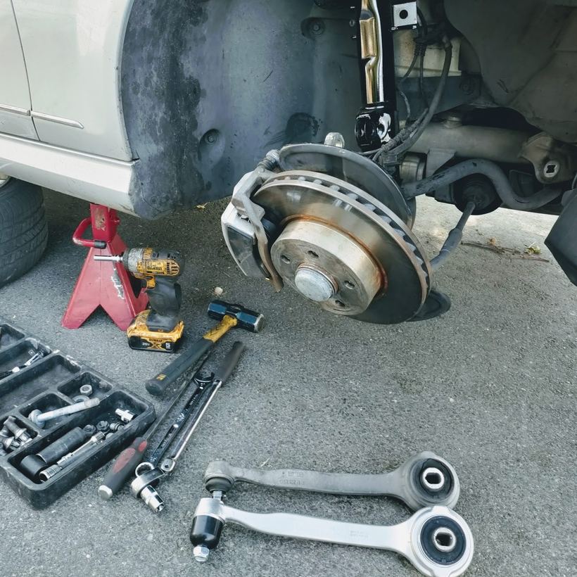 New control arms and a brake rotor on a car up on a jack stand