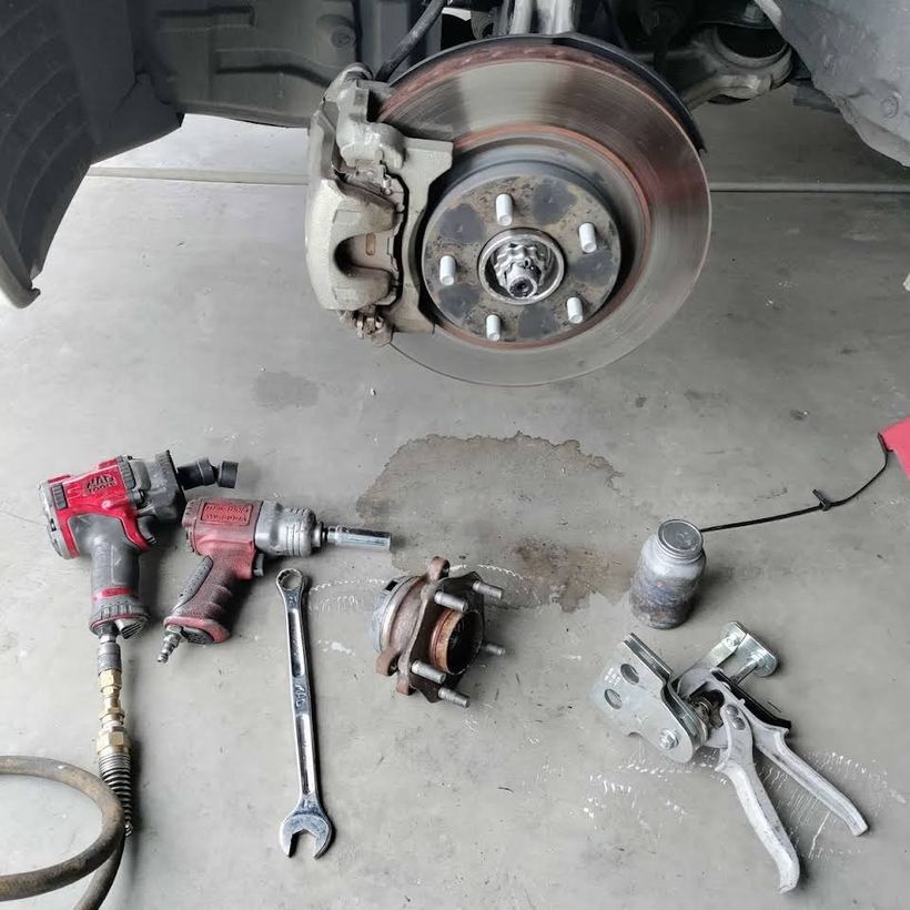 A wheel hub and brake rotor exposed, air tools and the old parts on the floor