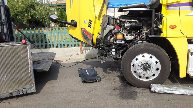 A yellow semi with the cab tilted, repaired at the curb